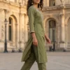 Woman wearing an olive green embroidered kurta and matching pants with embellished sandals, walking in a grand historic European courtyard.